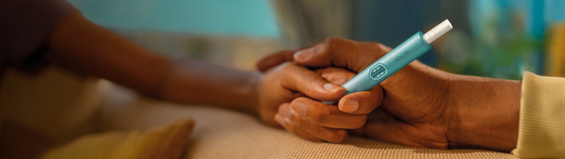 A woman holds an IQOS device while looking at a laptop.